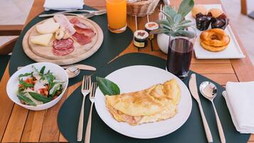 A breakfast setting with a plate of omelette, a bowl of salad, and a plate of assorted meats and cheeses.