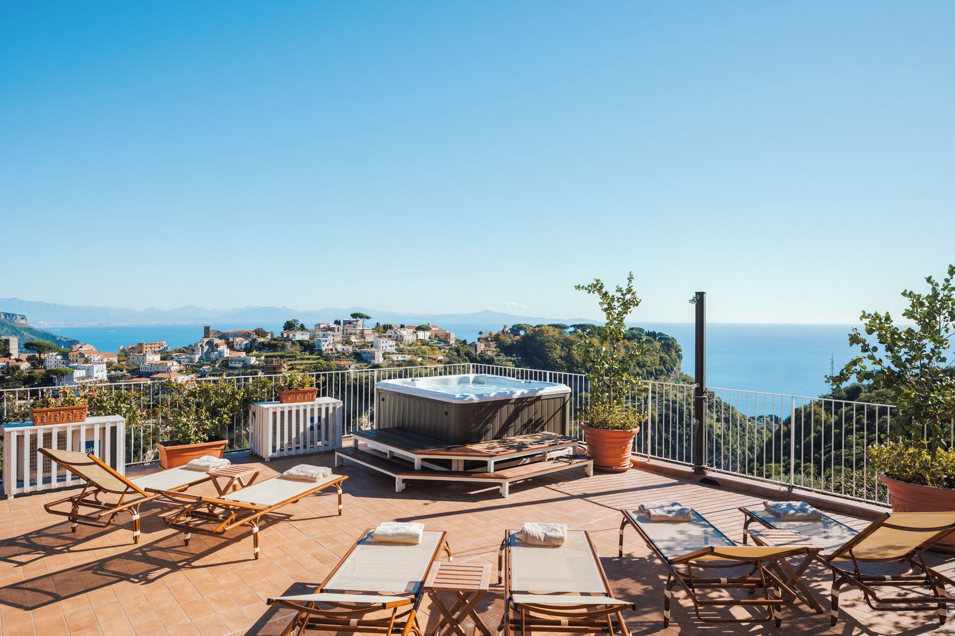 A rooftop terrace with sun loungers, a hot tub, and potted plants.