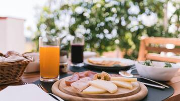 Un desayuno con una tabla de madera de quesos, jamón y pan, un vaso de zumo de naranja y una bebida oscura.