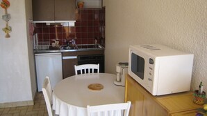 Une cuisine compacte avec une table et des chaises blanches, un four à micro-ondes et un petit réfrigérateur.