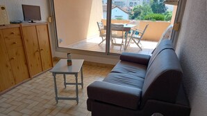 Un petit salon avec un canapé, une table et un téléviseur posé sur un meuble en bois.