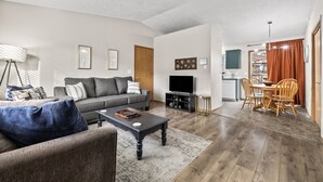 A modern living room with a sofa, coffee table, and TV. There is a dining area with a table and chairs. The room has wooden flooring and white walls. - Fenced Backyard | Near Mall & Hospitals (39) (Boise)