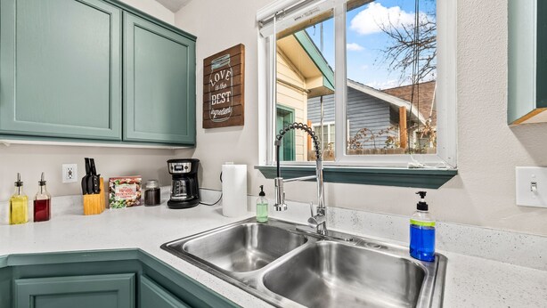 A kitchen with green cabinets, a stainless steel sink, a window with a view, and a sign that says "Love to the Best Ingredients". - Fenced Backyard | Near Mall & Hospitals (39) (Boise)