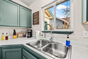 A kitchen with green cabinets, a stainless steel sink, a window with a view, and a sign that says "Love to the Best Ingredients". - Fenced Backyard | Near Mall & Hospitals (39) (Boise)