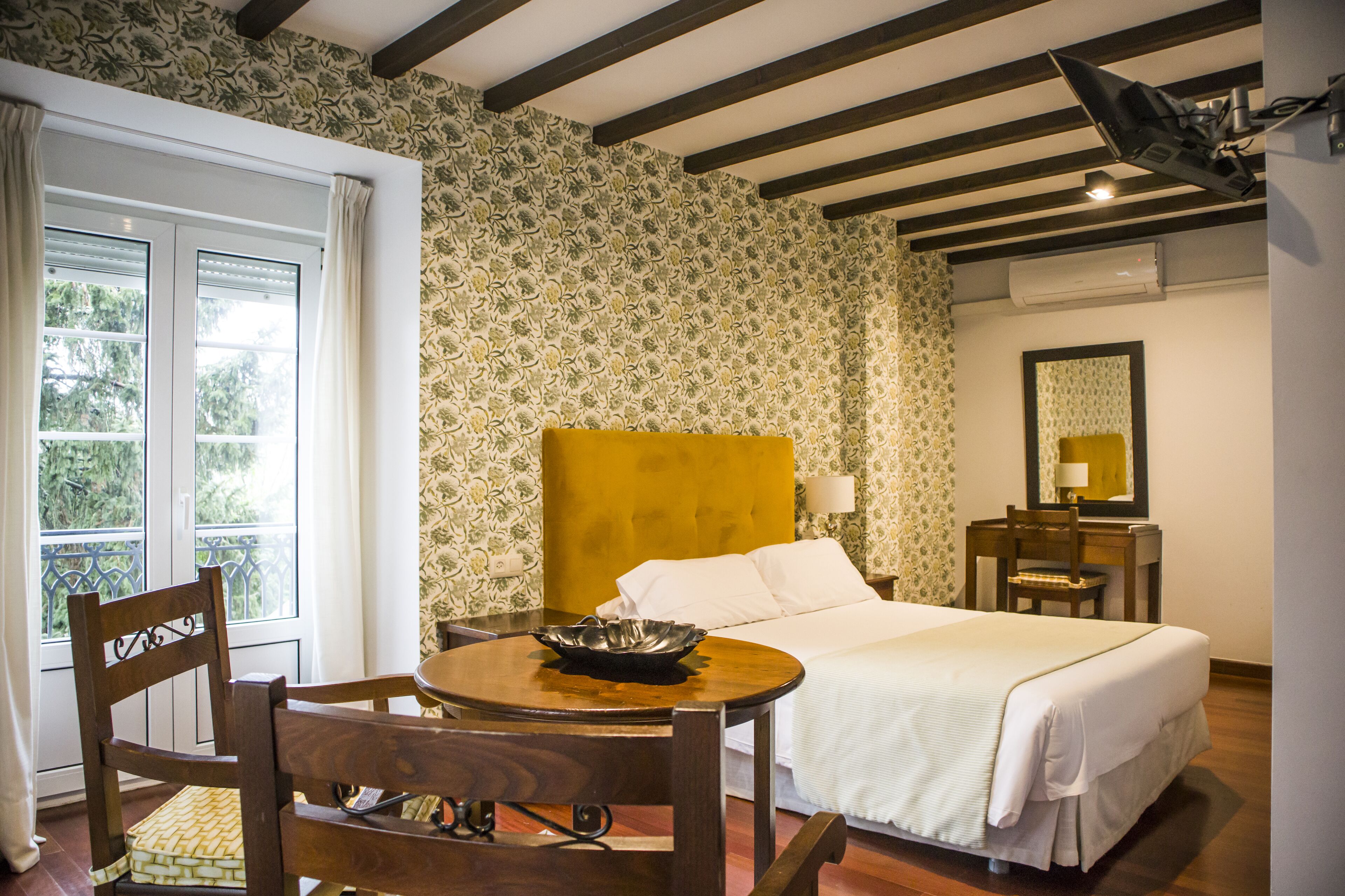 Habitación de hotel con cama, escritorio, silla, mesa con un tazón y ventana con cortinas.