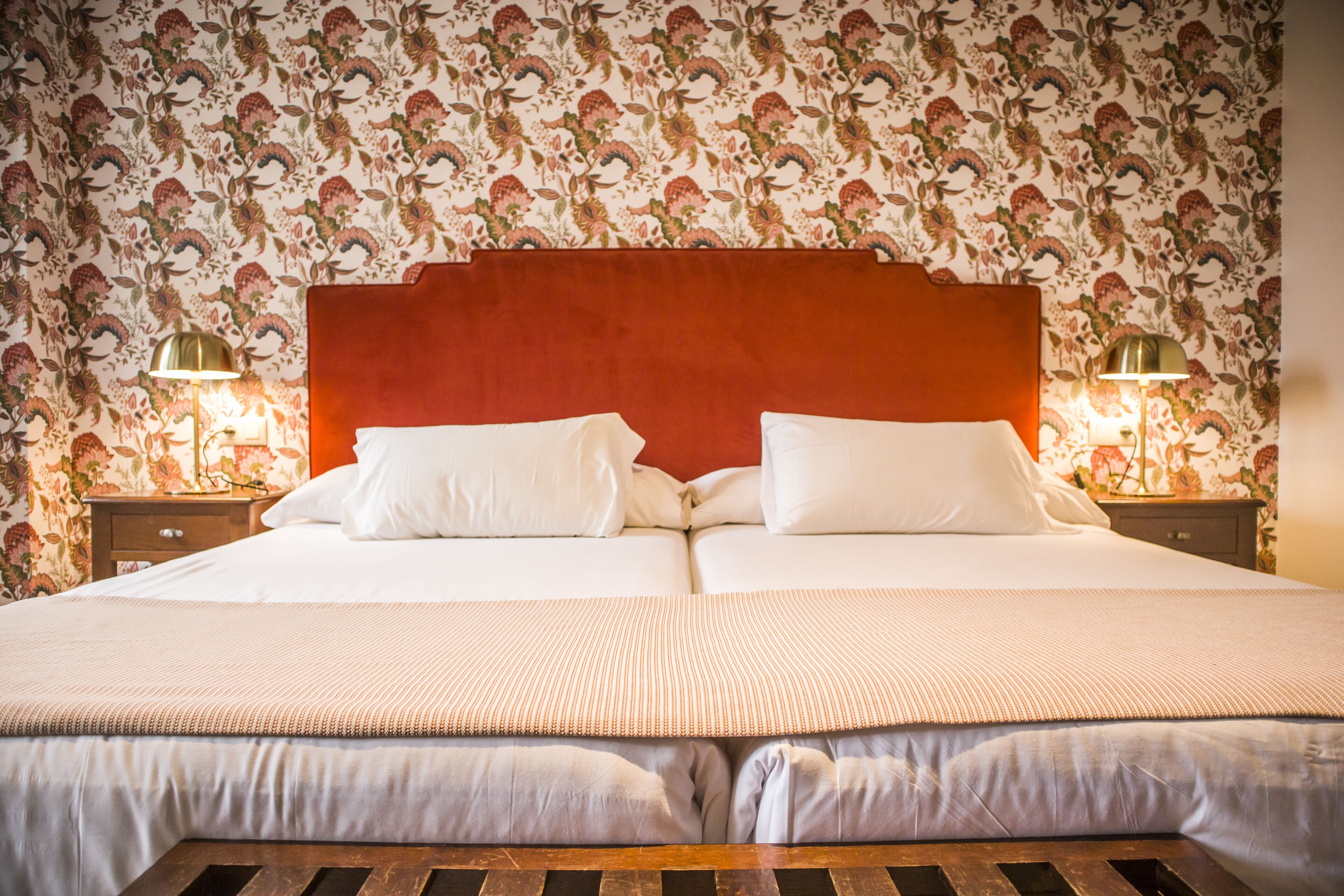 A double bed with a red headboard, two bedside tables with lamps, and floral wallpaper.