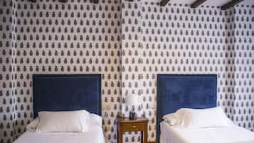 Een hotelkamer met twee bedden, een nachtkastje met een lamp, en behang met een patroon.