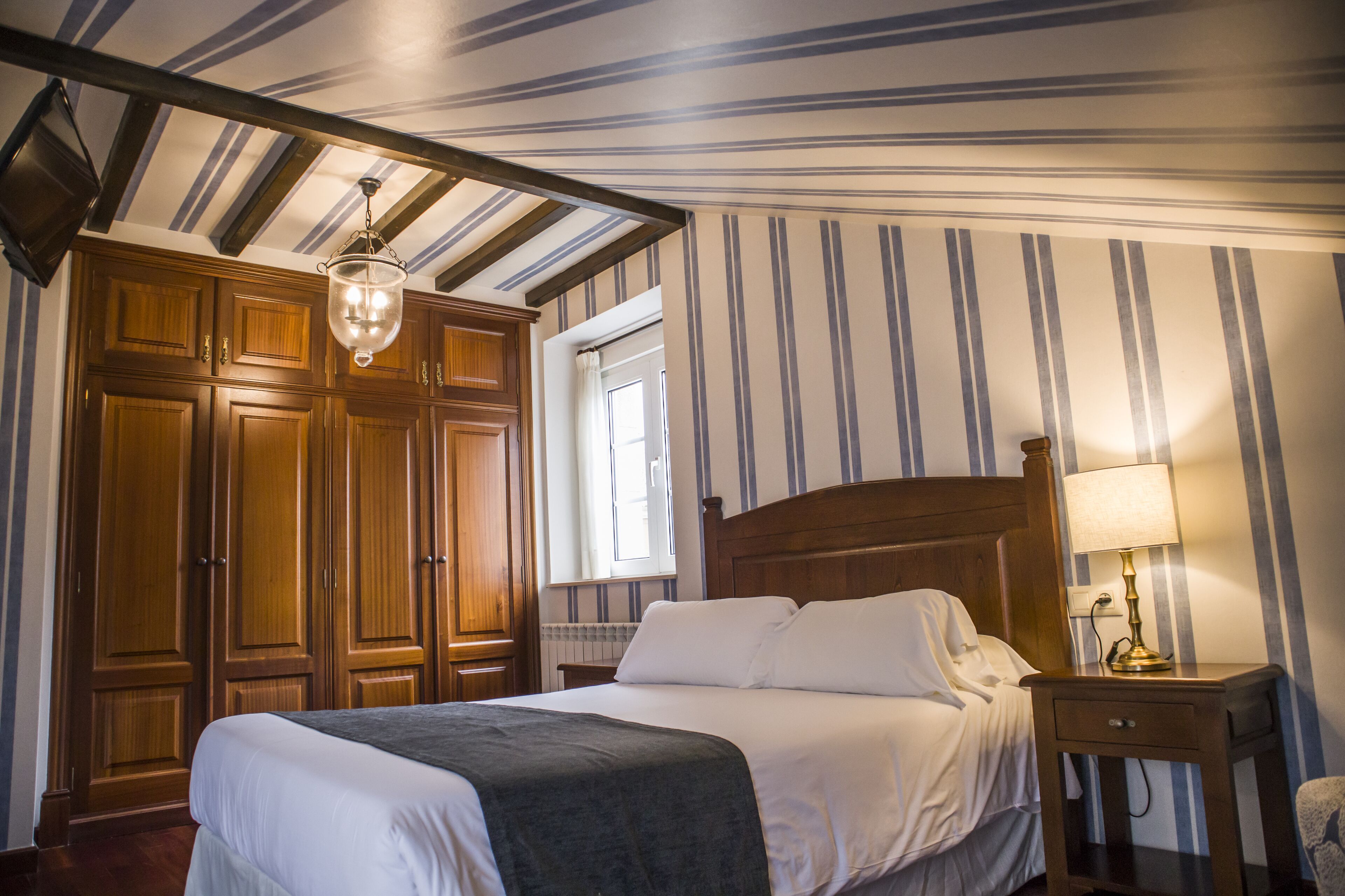 Una habitación de hotel con una cama grande, un armario de madera y una mesita de noche con lámpara.