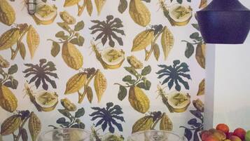A dessert display with various cakes and pastries, a fruit bowl, and a wall with a botanical pattern.