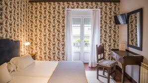 Habitación de hotel con cama, escritorio, silla, televisión y balcón con vistas.