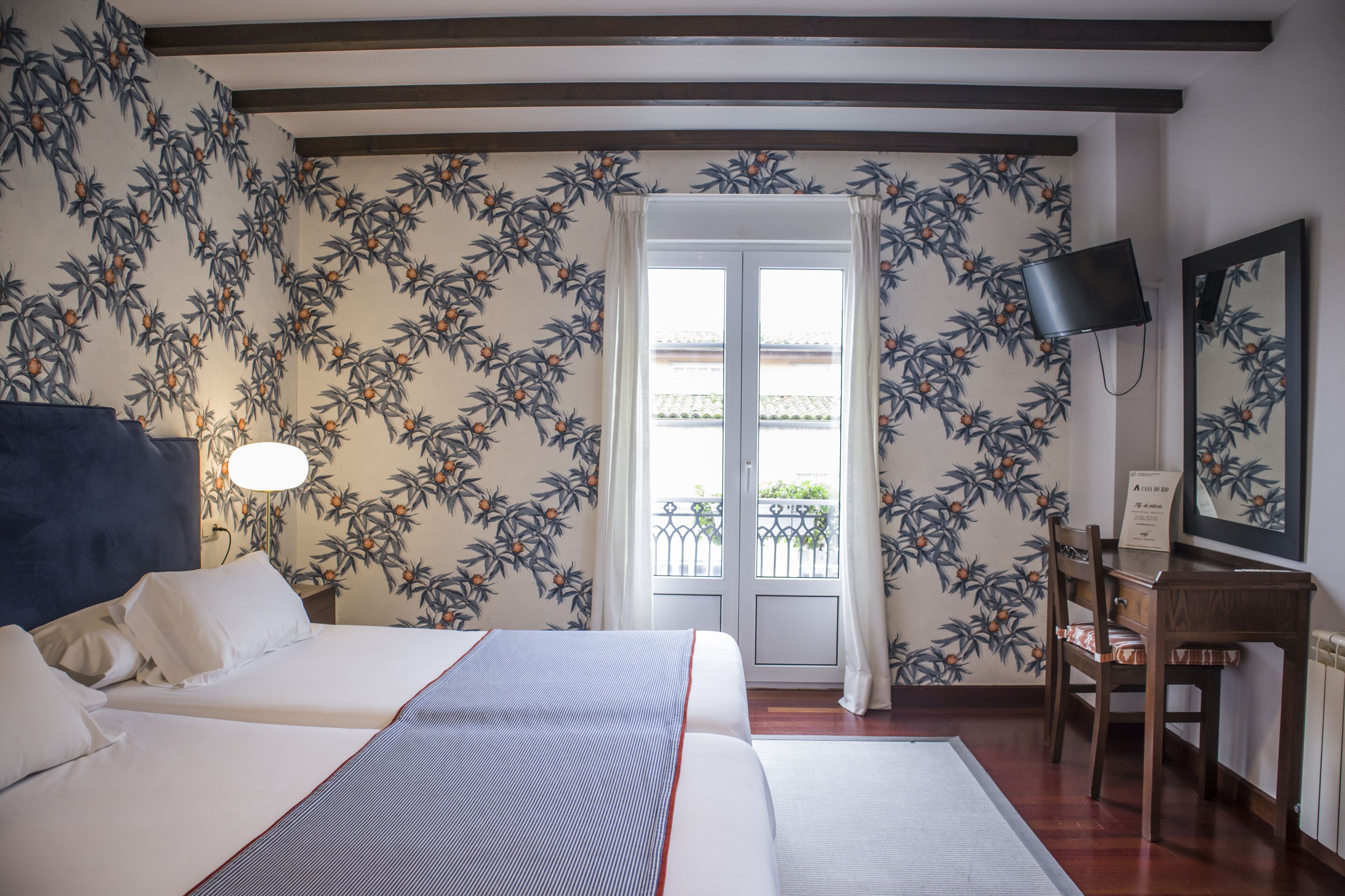 A hotel room with a bed, a desk, a chair, a TV, and a balcony with a view.