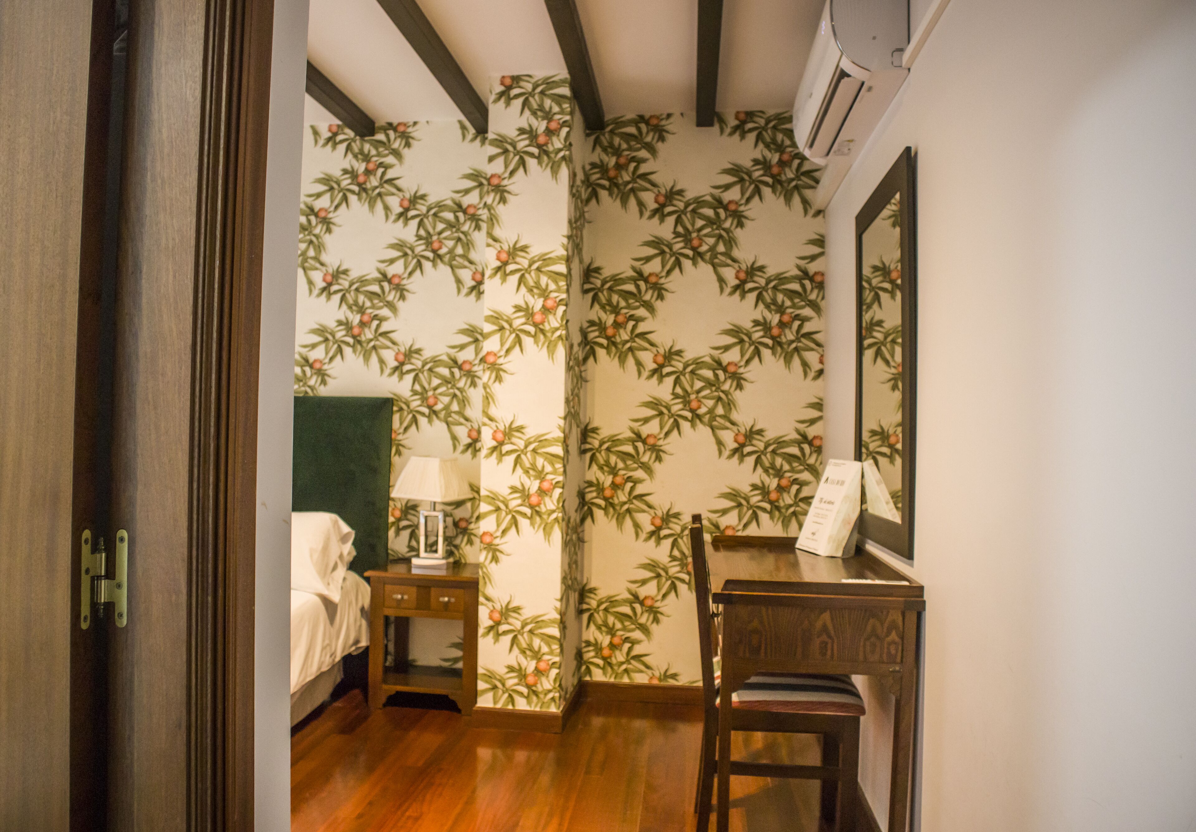 Een hotelkamer met een bed, nachtkastje met een lamp, een stoel en een spiegel aan de muur.