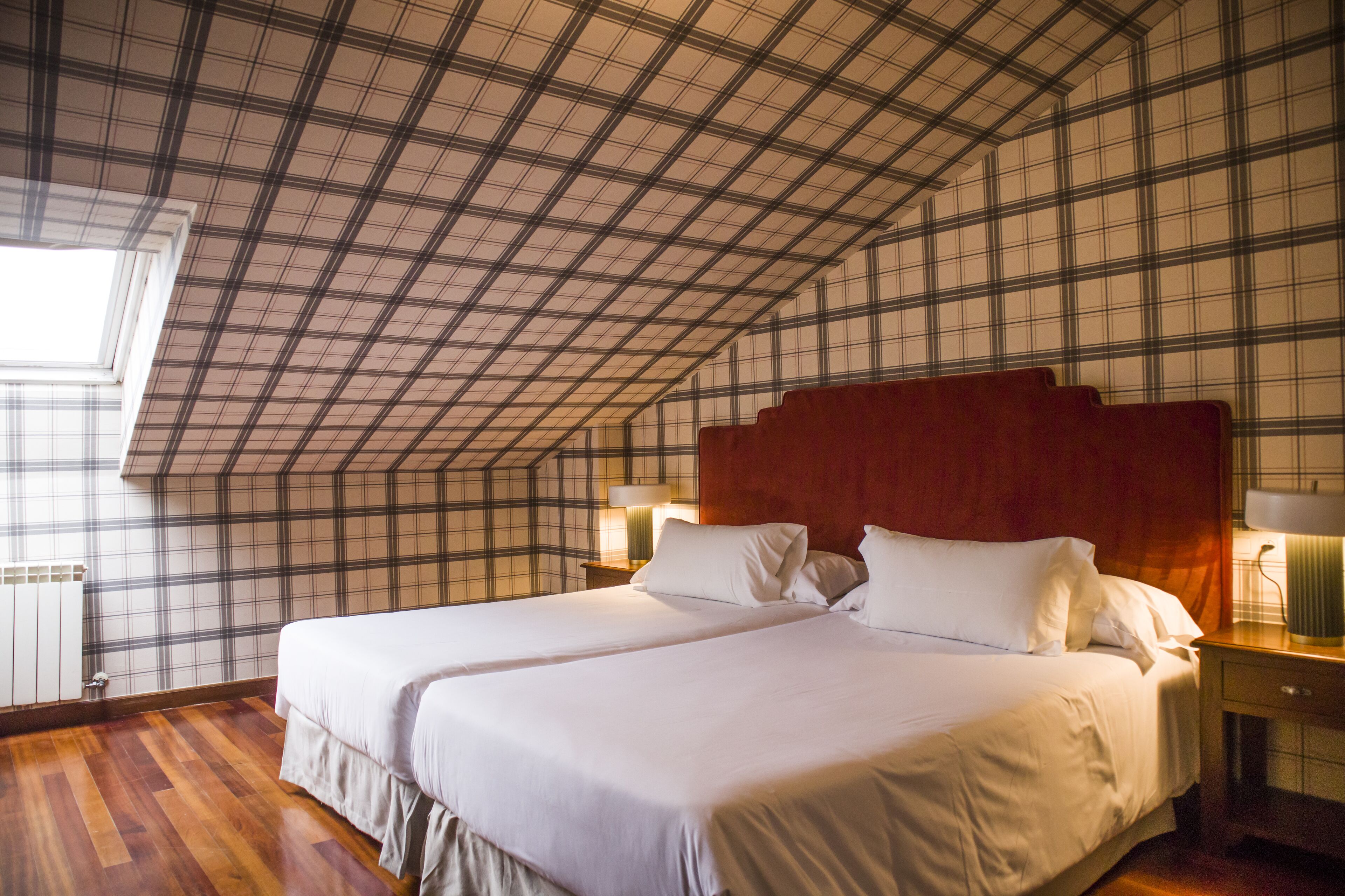Een slaapkamer met een groot bed, een houten vloer, een geruit plafond en een raam.