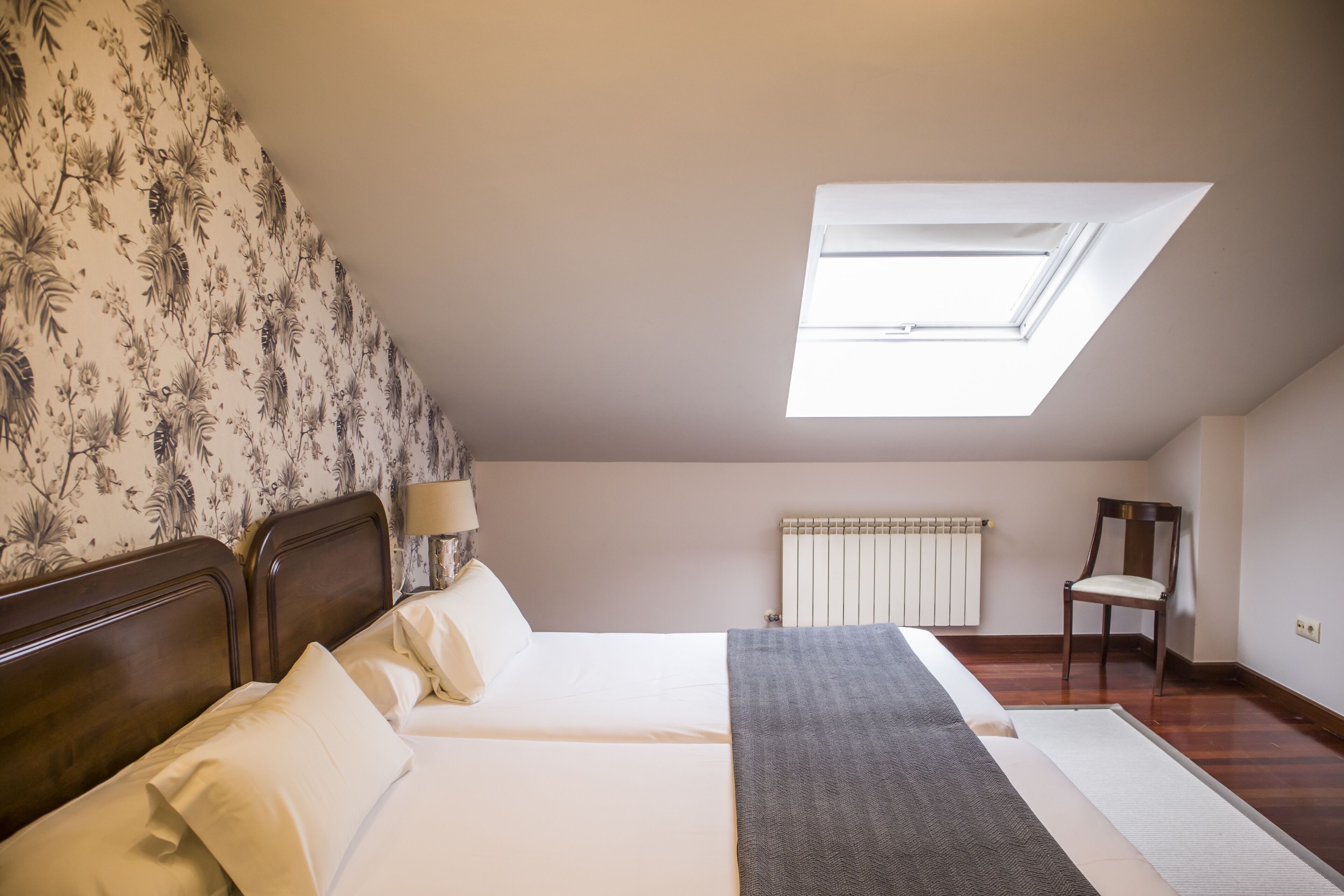 Een slaapkamer met dakraam, een bed met witte lakens, een stoel en een radiator.