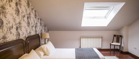 A bedroom with a skylight, a bed with white linens, a chair, and a radiator.
