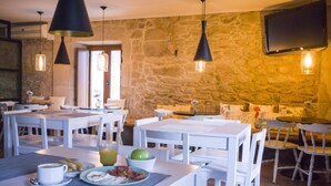 Un comedor con mesas y sillas blancas, paredes de piedra e iluminación colgante.