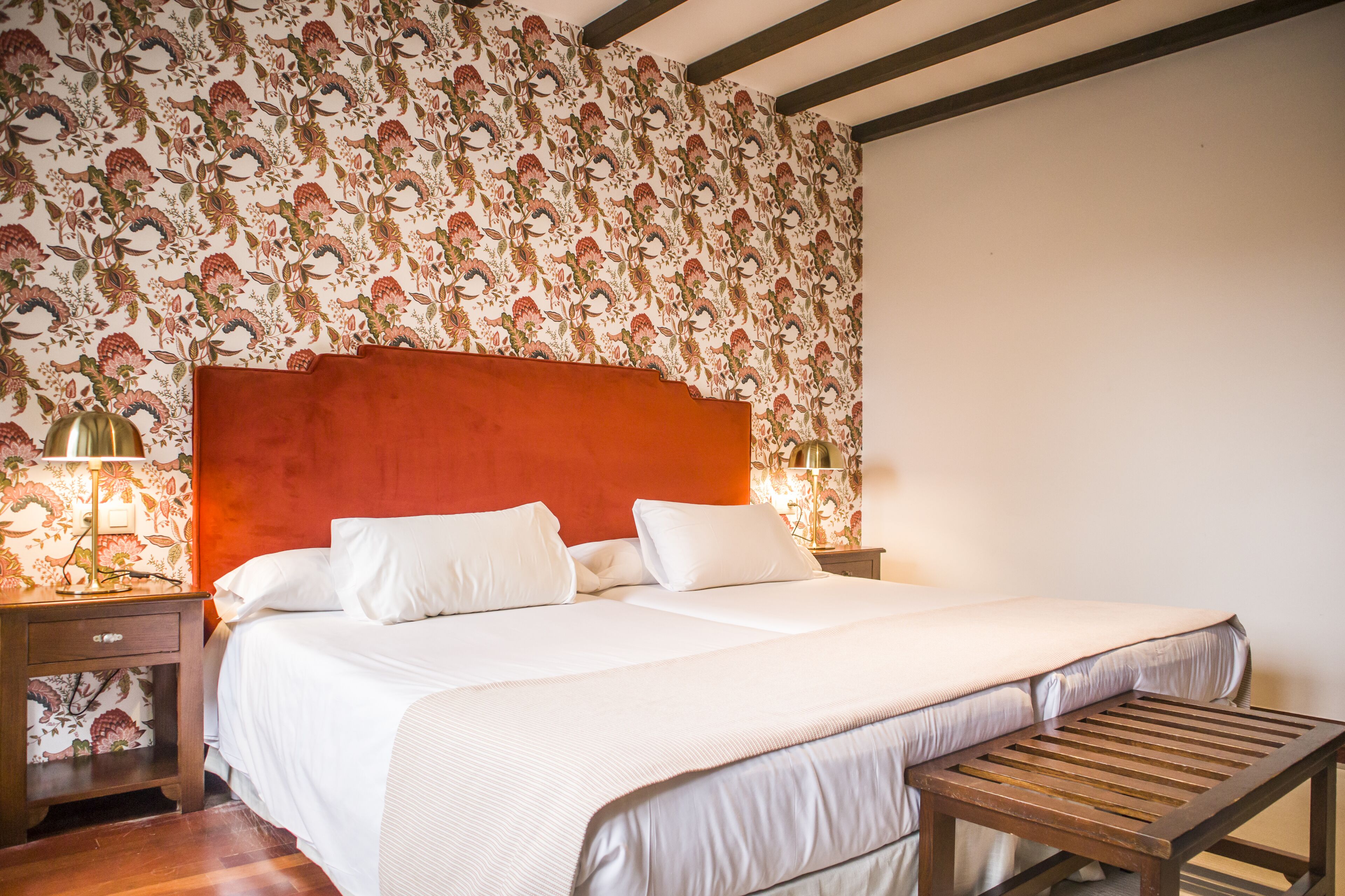 A double bed with white linens, a wooden headboard, and a nightstand with a lamp.