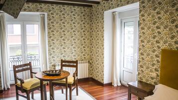 Een kamer met houten vloer, een eettafel met stoelen, een radiator en een bed met hoofdeinde.