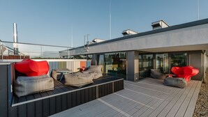 A rooftop deck with modern seating, a glass-enclosed area, and a clear sky. - The Brucklyn Apartments (Erlangen)