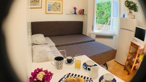 Een slaapkamer met een bed, een tafel met ontbijtartikelen, een raam met uitzicht op groen en een televisie op een standaard.