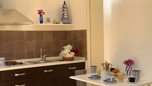 Een moderne keuken met een inbouwfornuis, een spoelbak en een wit aanrecht. Er staat een klein tafeltje met een mand vol bloemen en een kan sap.