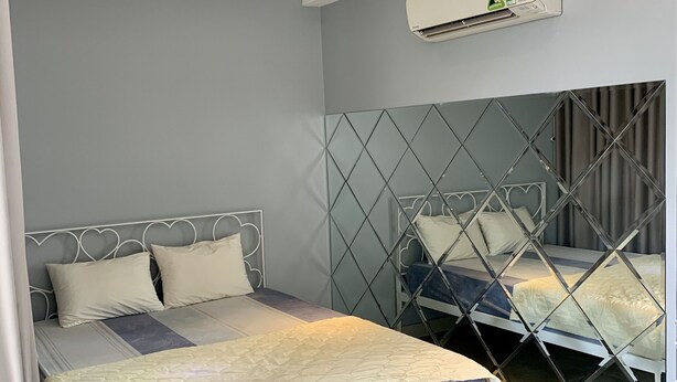 A modern bedroom with a bed, a second bed, a decorative wall panel, and an air conditioning unit. - Bao Ngoc Hotel (Ho Chi Minh City)