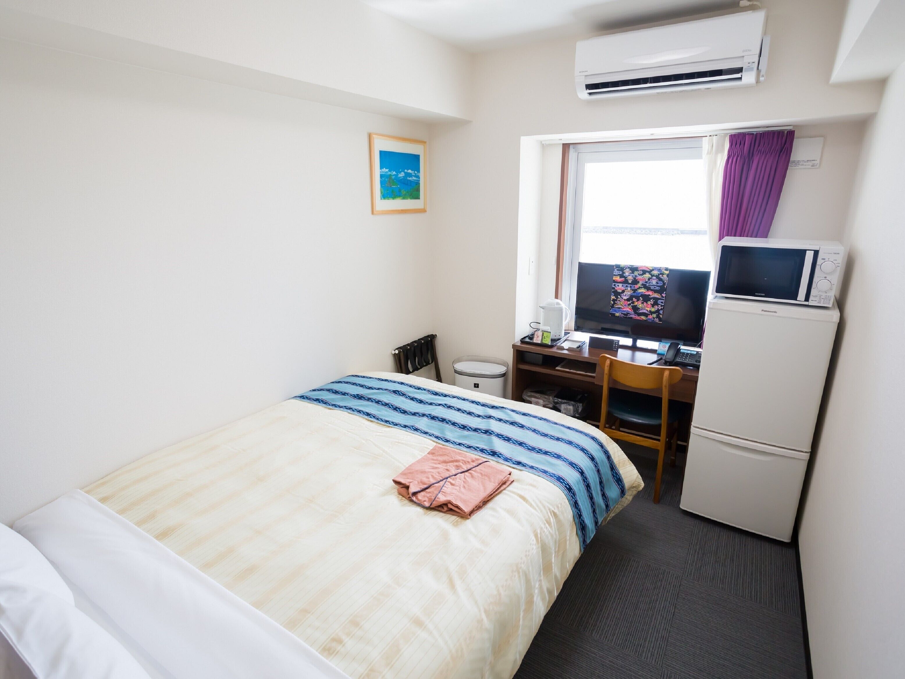 Una habitación de hotel con una cama, un escritorio con computadora, un microondas y aire acondicionado.