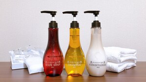 Three bottles of body care products, a box of toiletries, and a stack of towels on a wooden surface. - Hotel Peace Island Nago (Nago)