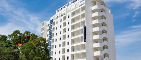 A multi-story hotel with a white facade, multiple balconies, and a clear sky.