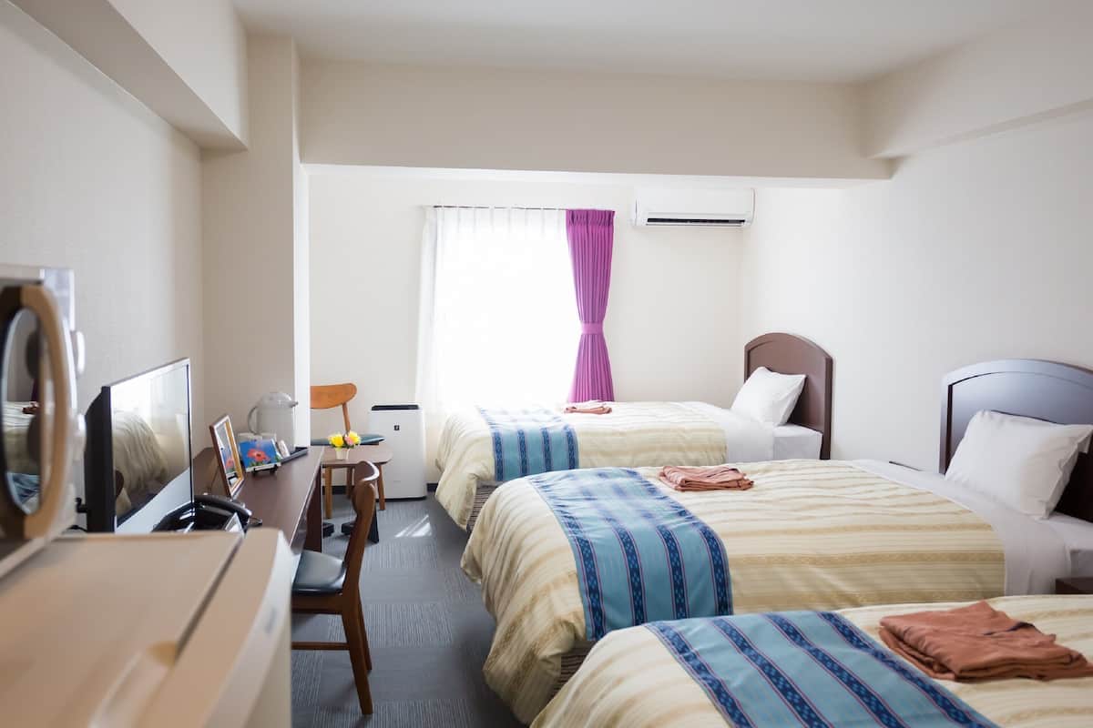 A hotel room with two beds, a desk with a chair, a TV, and an air conditioning unit.