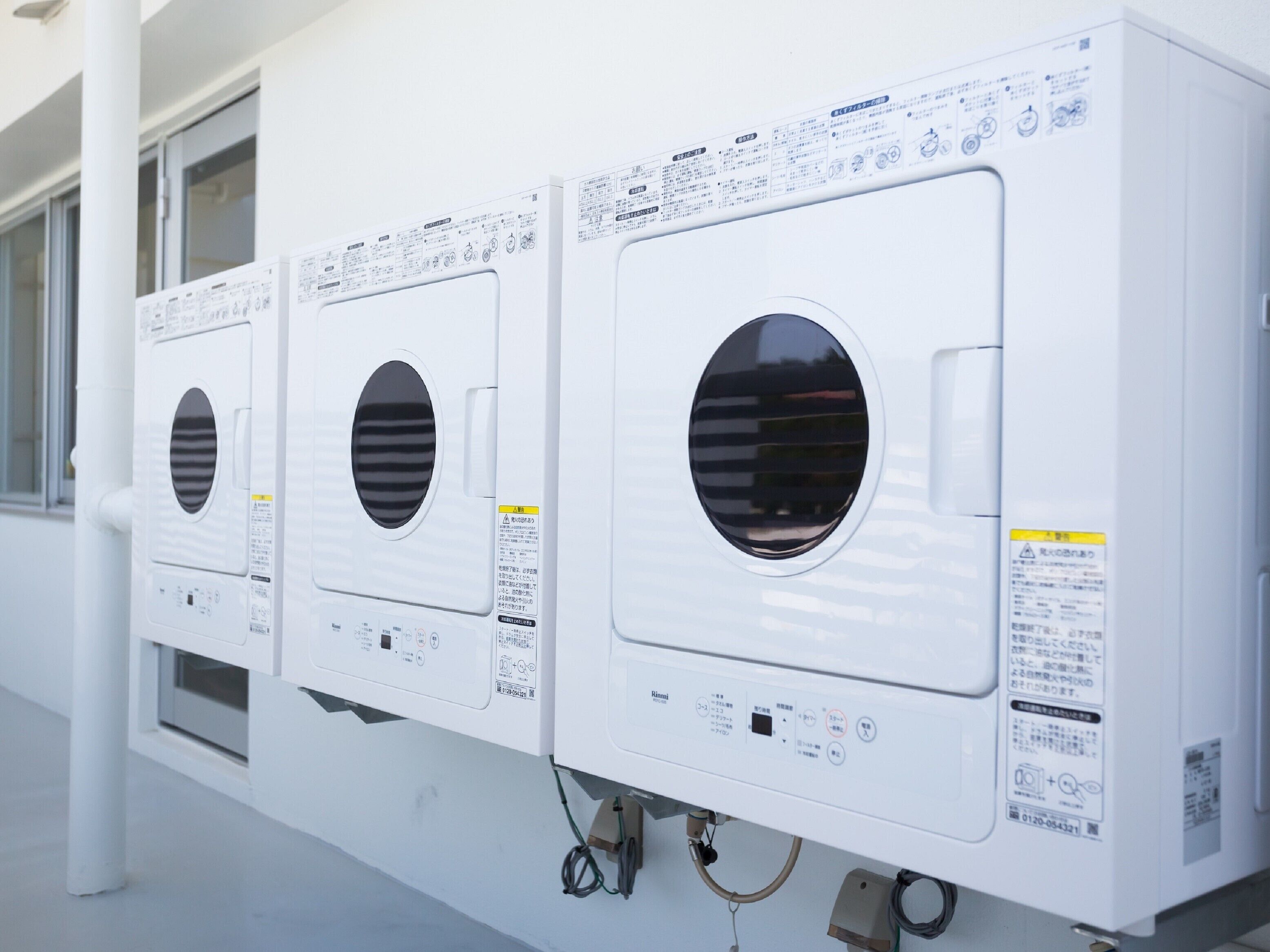 Une rangée de machines à laver blanches, dotées de panneaux de commande et d’instructions de sécurité.