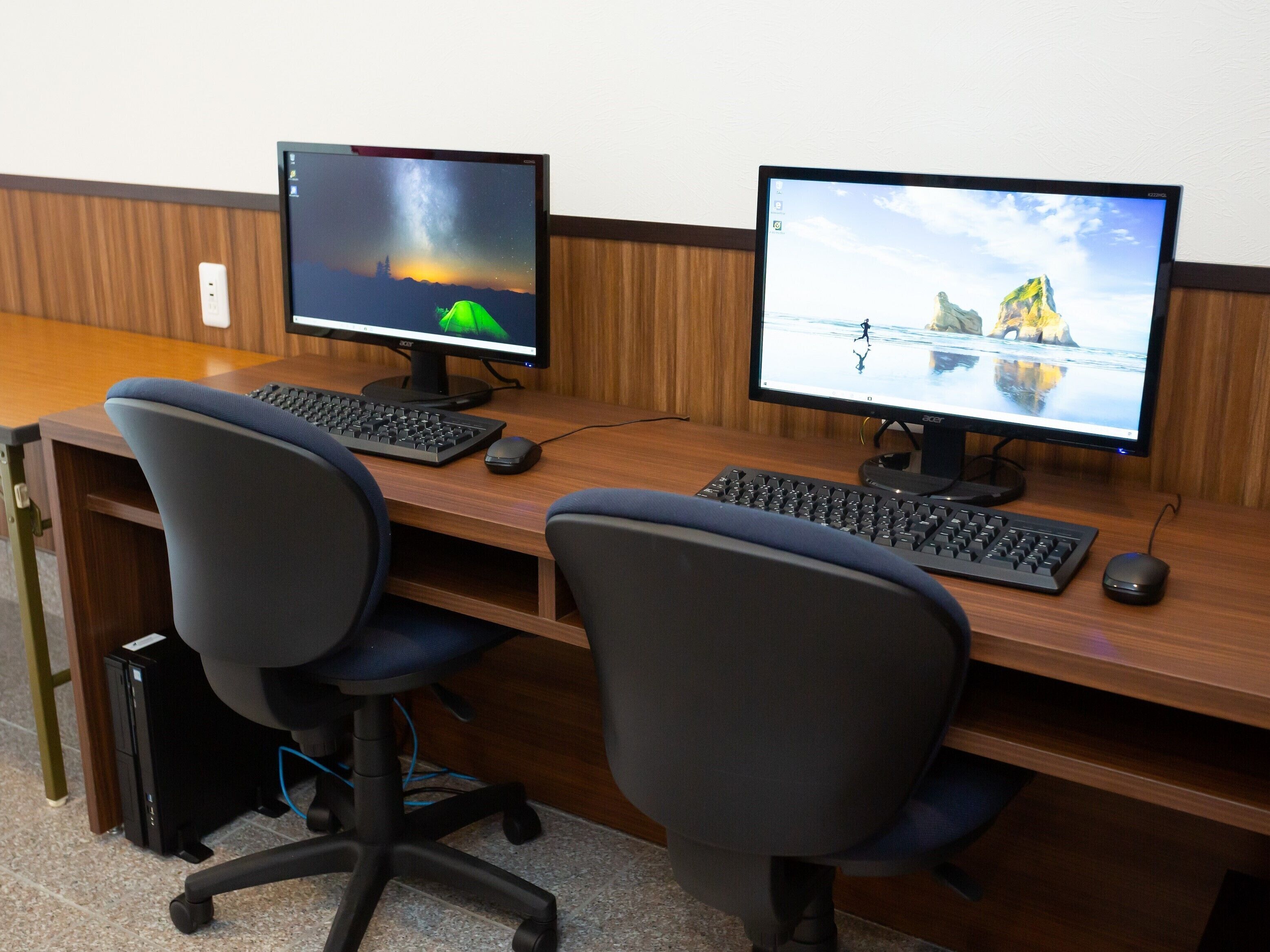 Un espacio de trabajo con dos monitores, dos teclados y dos sillas de oficina.