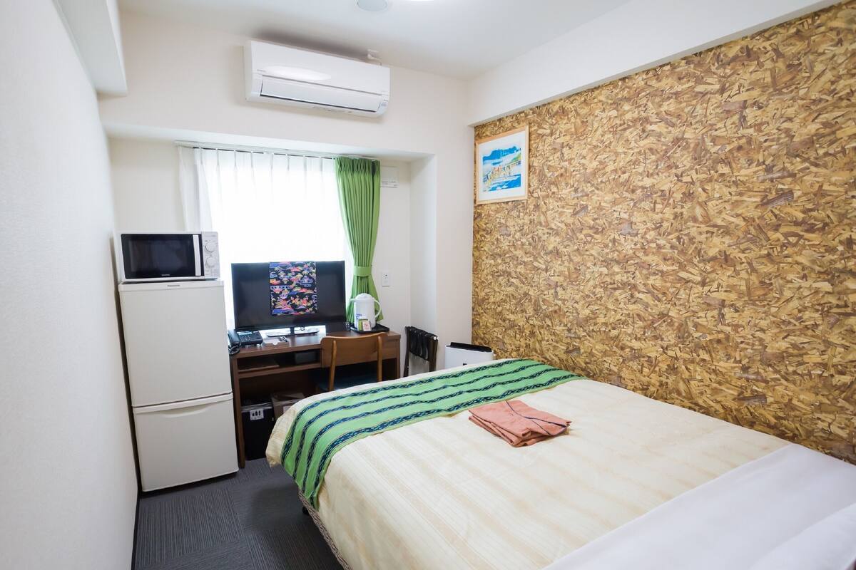 A hotel room with a bed, a desk with a computer, a microwave, and an air conditioner.