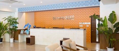 A hotel reception area with a reception desk, seating area, and potted plants.