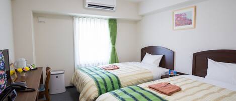 A hotel room with two beds, a desk with a telephone, a chair, a waste bin, and a window with curtains.