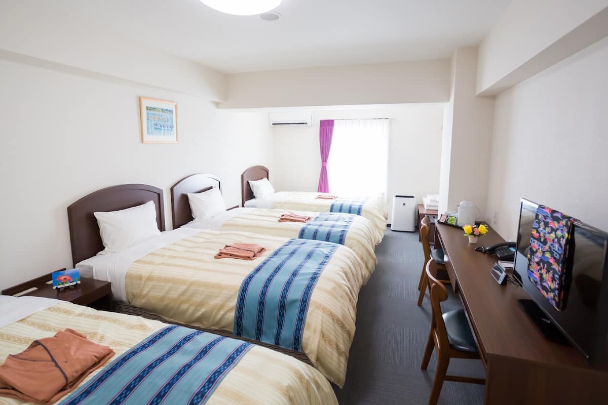 A hotel room with three beds, a desk with a computer, a TV, and a coffee maker.