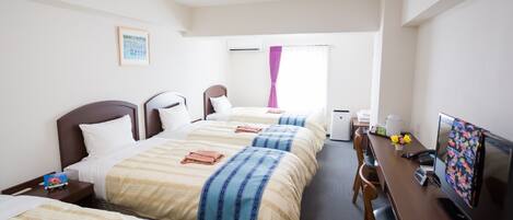 Una habitación de hotel con tres camas, un escritorio con computadora, televisión y cafetera.