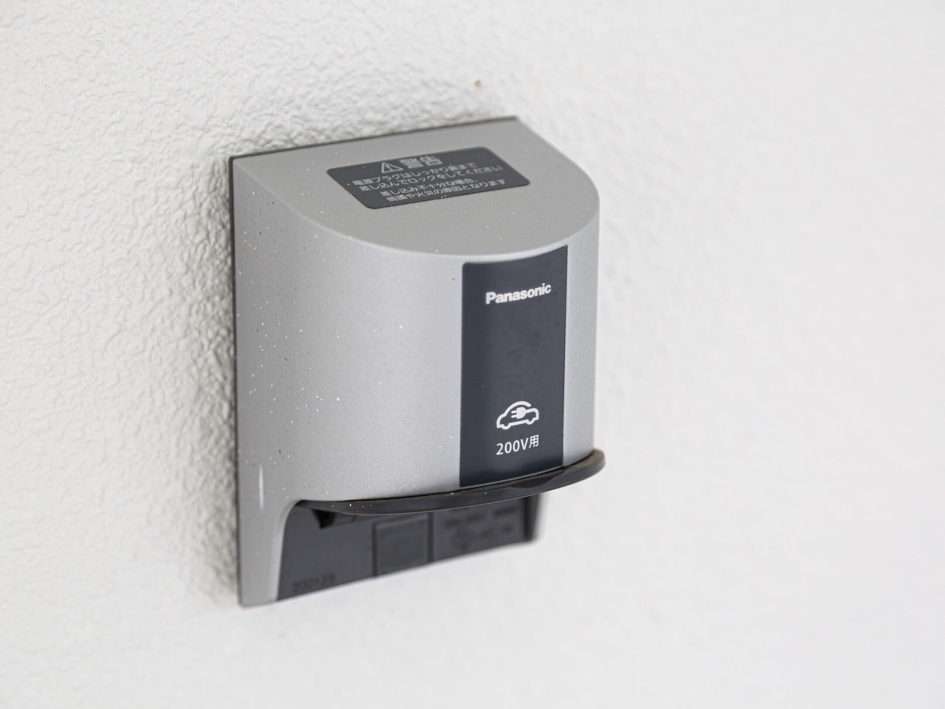 A 200V electric car charging station by Panasonic mounted on a textured wall.