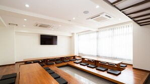 A conference room with a long table and benches, a flat-screen TV on the wall, and large windows with sheer curtains. - Hotel Peace Island Nago (Nago)