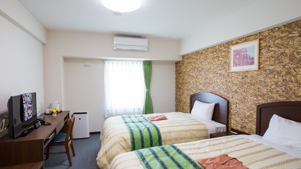 A hotel room with two beds, a desk with a computer, a small air conditioning unit, and a window with curtains. - Hotel Peace Island Nago (Nago)