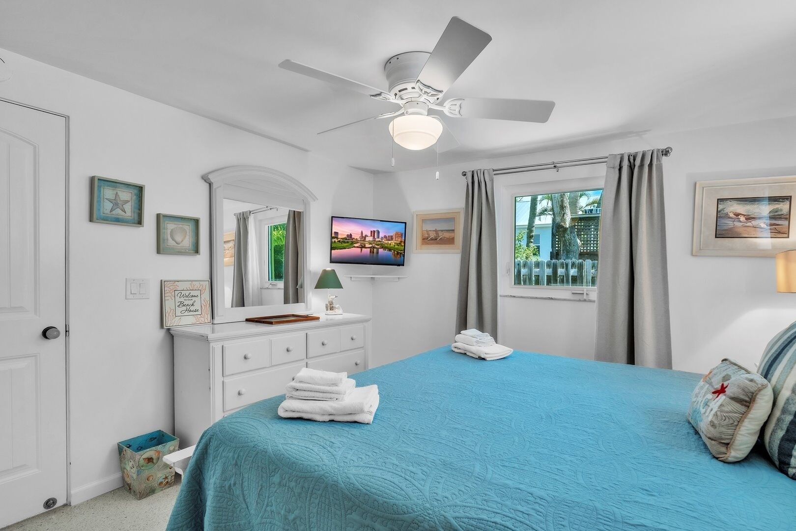 A bedroom with a bed, a ceiling fan, a TV, a dresser, and a window with curtains.