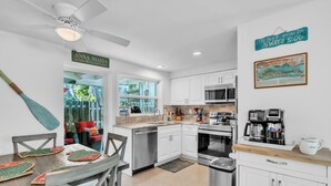 Una cocina moderna con armarios blancos, electrodomésticos de acero inoxidable y un comedor con mesa y sillas de madera.