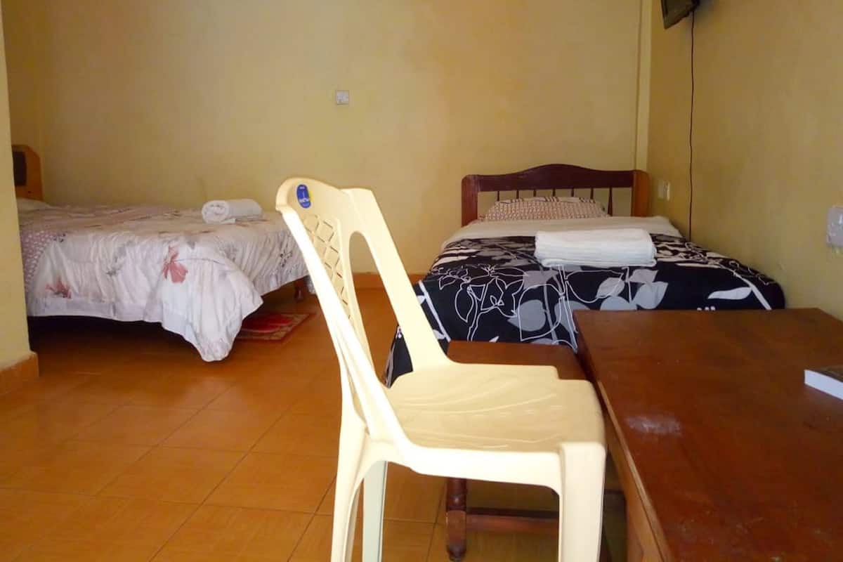A room with two beds, a wooden table, a plastic chair, and a television mounted on the wall.