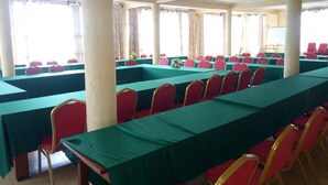Una sala de conferències amb files de taules i cadires, grans finestres i una pissarra.