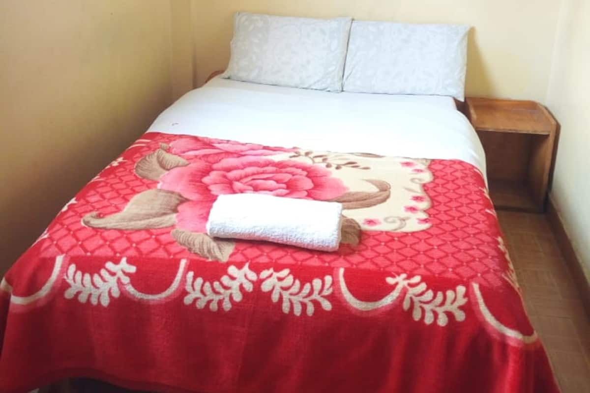 A single bed with a red and white bedspread, a white canopy, and a wooden nightstand.