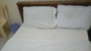 A bed with white bedding, a wooden headboard, and a blue trash bin beside it. - Caldera Suites (Nakuru)