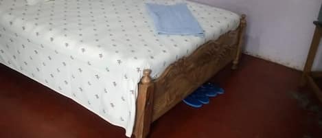 Una cama individual con estructura de madera y cubrecama blanco estampado con motivos florales.