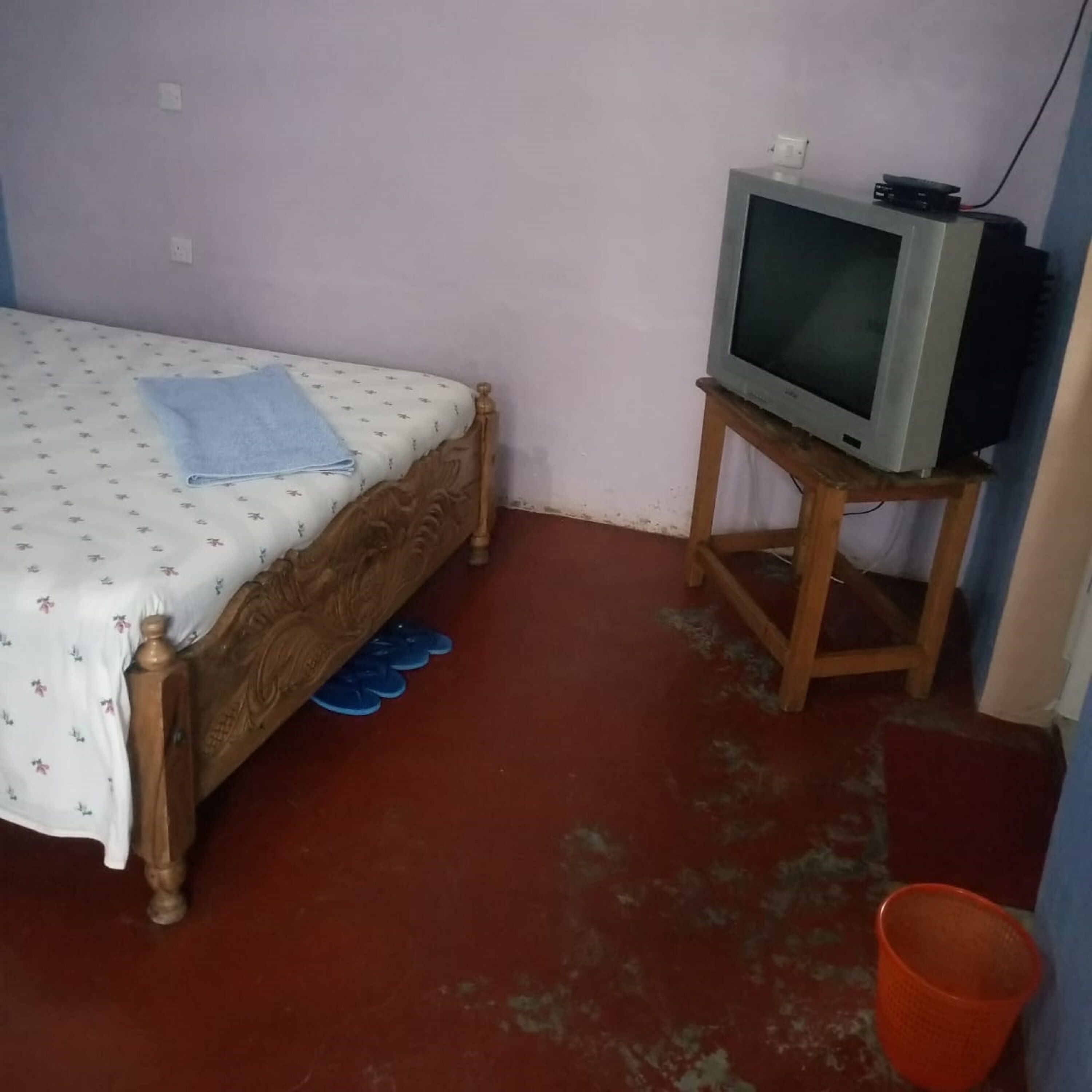 A bedroom with a bed, a television on a wooden stand, and a red bucket.