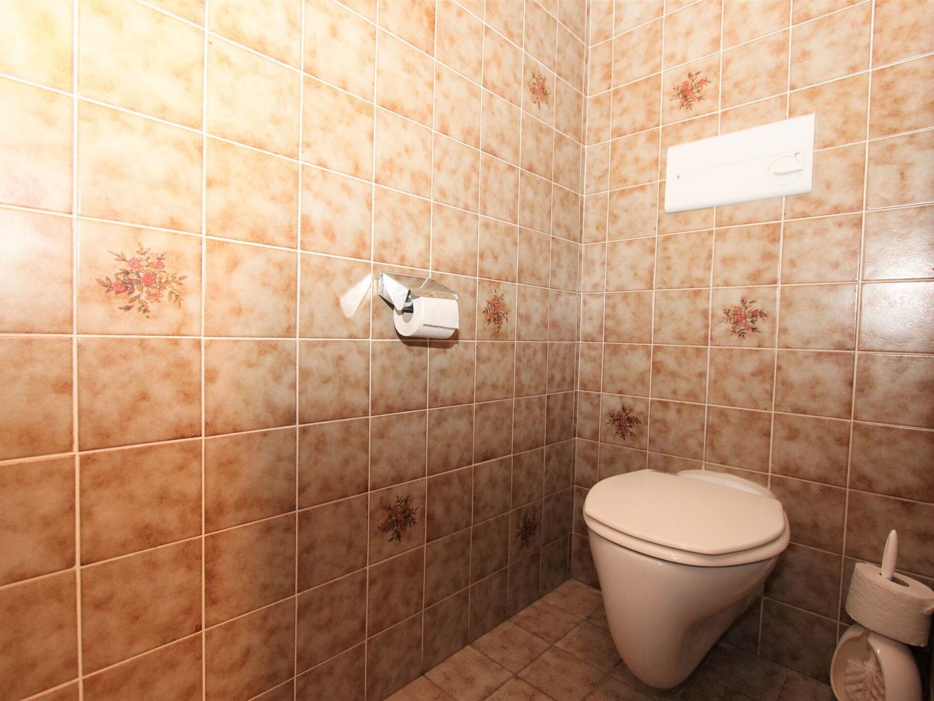 A bathroom with beige tiles, a toilet, and a paper towel dispenser.