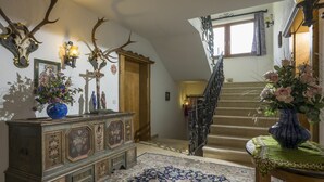 A grand staircase with ornate railings, a wooden cabinet with religious statues, and a patterned rug. - Beautiful apartment for 2 people with WIFI, TV, balcony, pets allowed and panoramic view (Fügen)